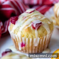 A whole cranberry muffin with glaze on top resting on a white marble surface.