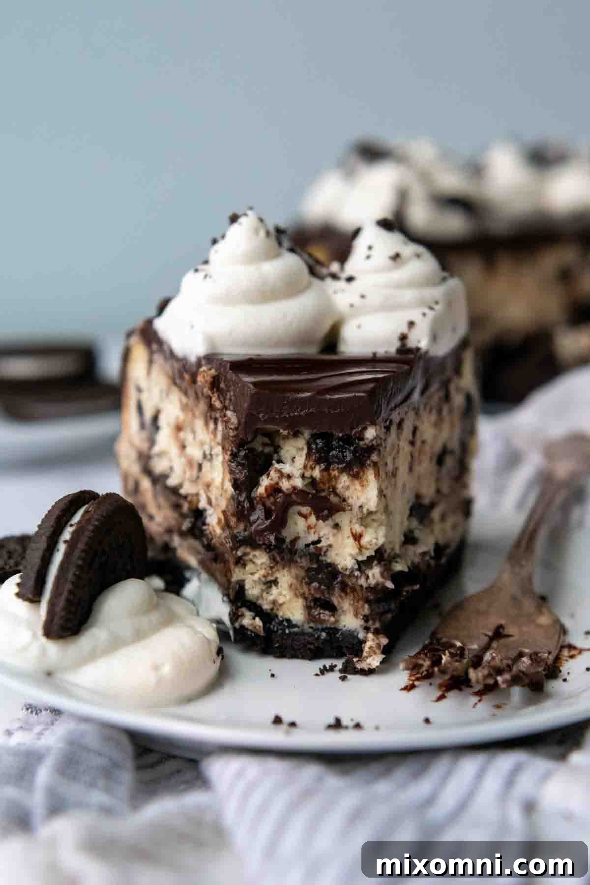 a slice of gluten free oreo cheesecake with a bite taken out on a white plate.