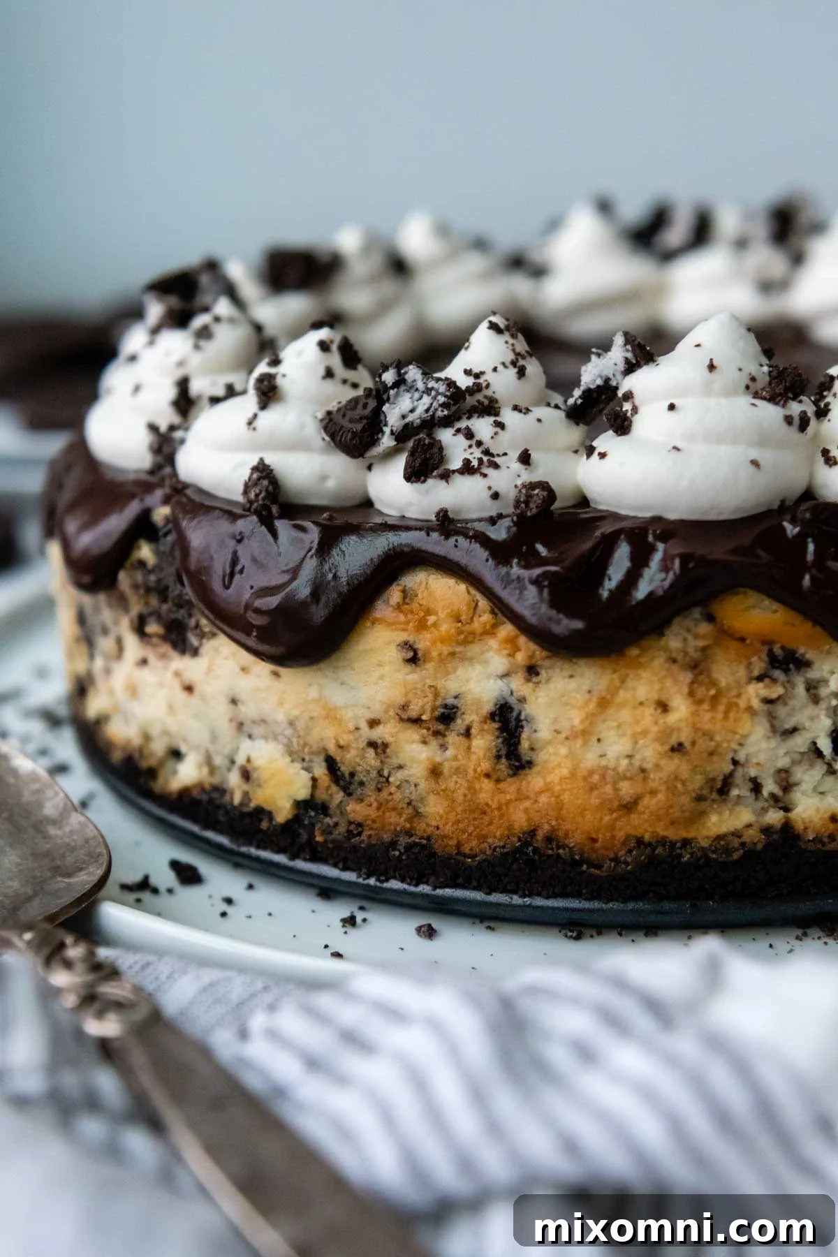 an uncut gluten free oreo cheesecake with ganache and whipped cream on top.