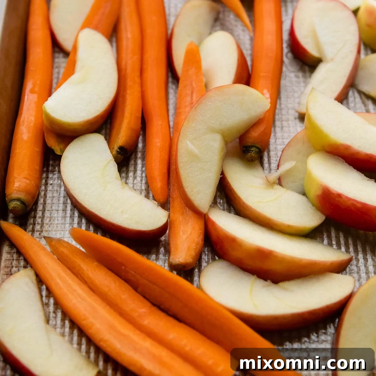 Raw, cut carrots and apples arranged on a baking pan, ready for glazing and roasting.