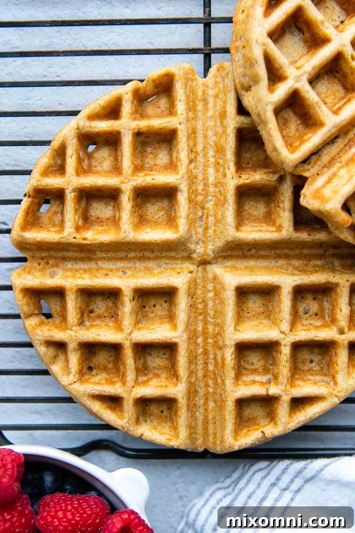 a oat flour waffle on a cooling rack with berries next to it.