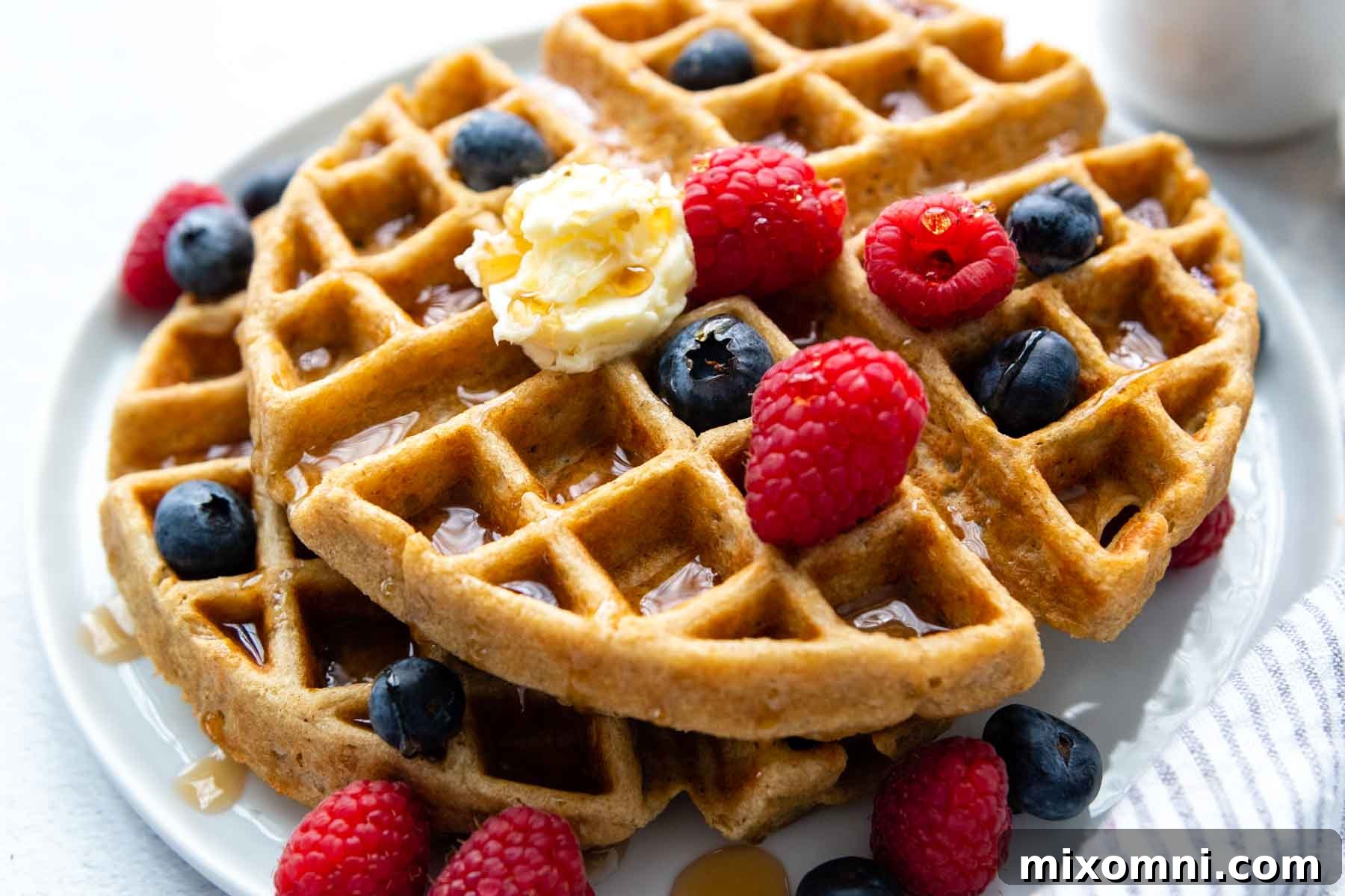 a stack of waffles on a white plate with berries, butter and syrup.