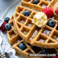 overhead show of oat flour waffles with fresh berries, syrup and butter.