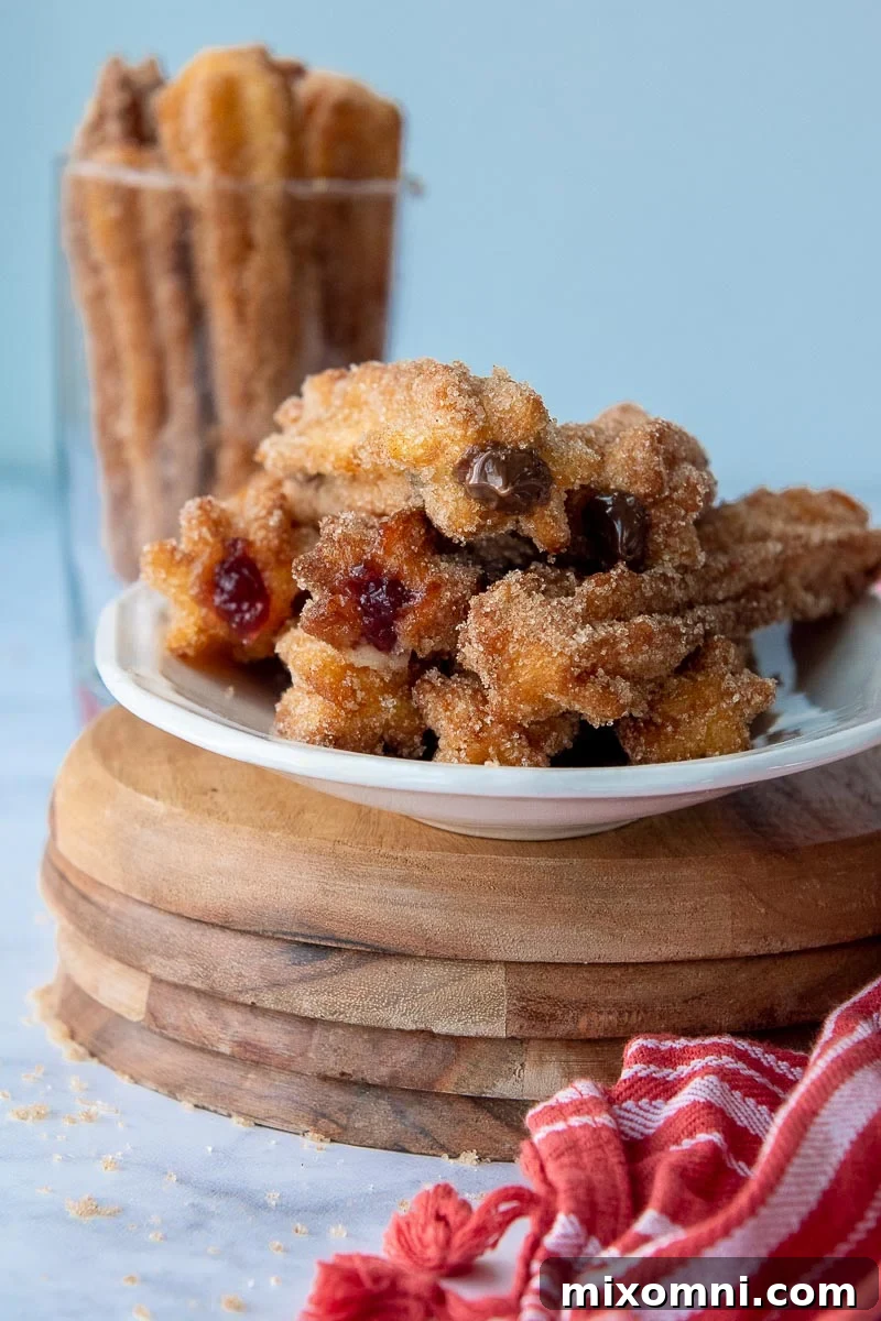 A plate brimming with golden-brown, cinnamon-sugar-dusted stuffed churros, perfectly fried and ready to enjoy. A cozy red kitchen towel rests beside the plate.