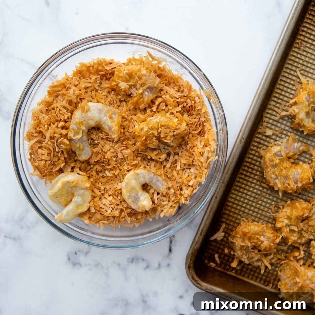 A close-up shot of shrimp being carefully dipped and rolled in toasted coconut flakes, showcasing the breading process for gluten-free coconut shrimp.