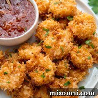 A plate of perfectly cooked gluten-free coconut shrimp with a side of dipping sauce, showcasing the golden crust and succulent interior.