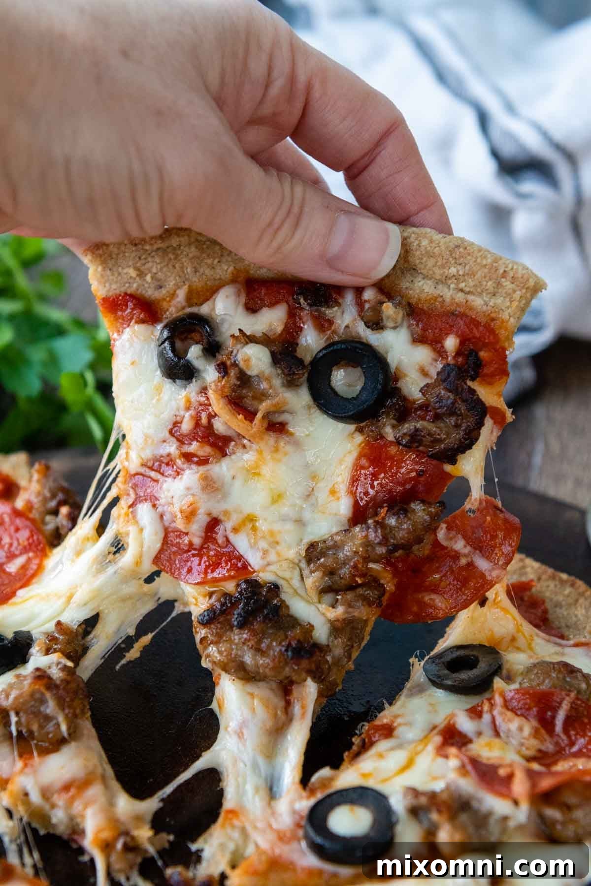 A delectable slice of almond flour pizza being pulled from the main pie, with rich, melted cheese stretching and dripping down, showcasing the perfect texture and inviting appeal of the crust.