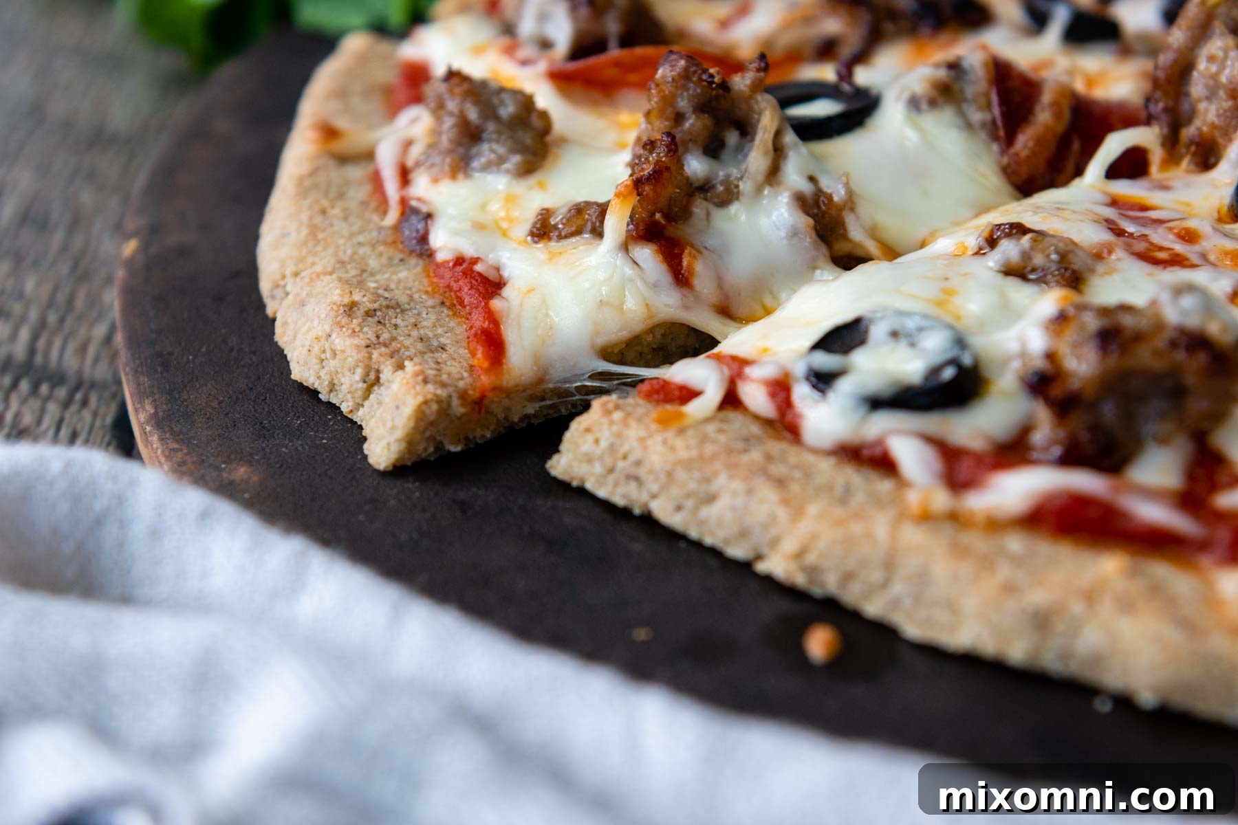 A close-up view of a freshly baked almond flour pizza, perfectly golden and crispy on a pizza stone, laden with melted cheese and delicious toppings.