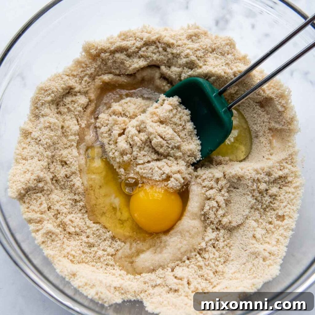 Wet ingredients including eggs and oil being mixed into the dry almond flour mixture.