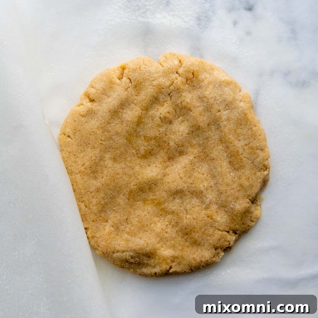 Almond flour pizza dough patted into a thick, uniform disc shape between parchment papers.