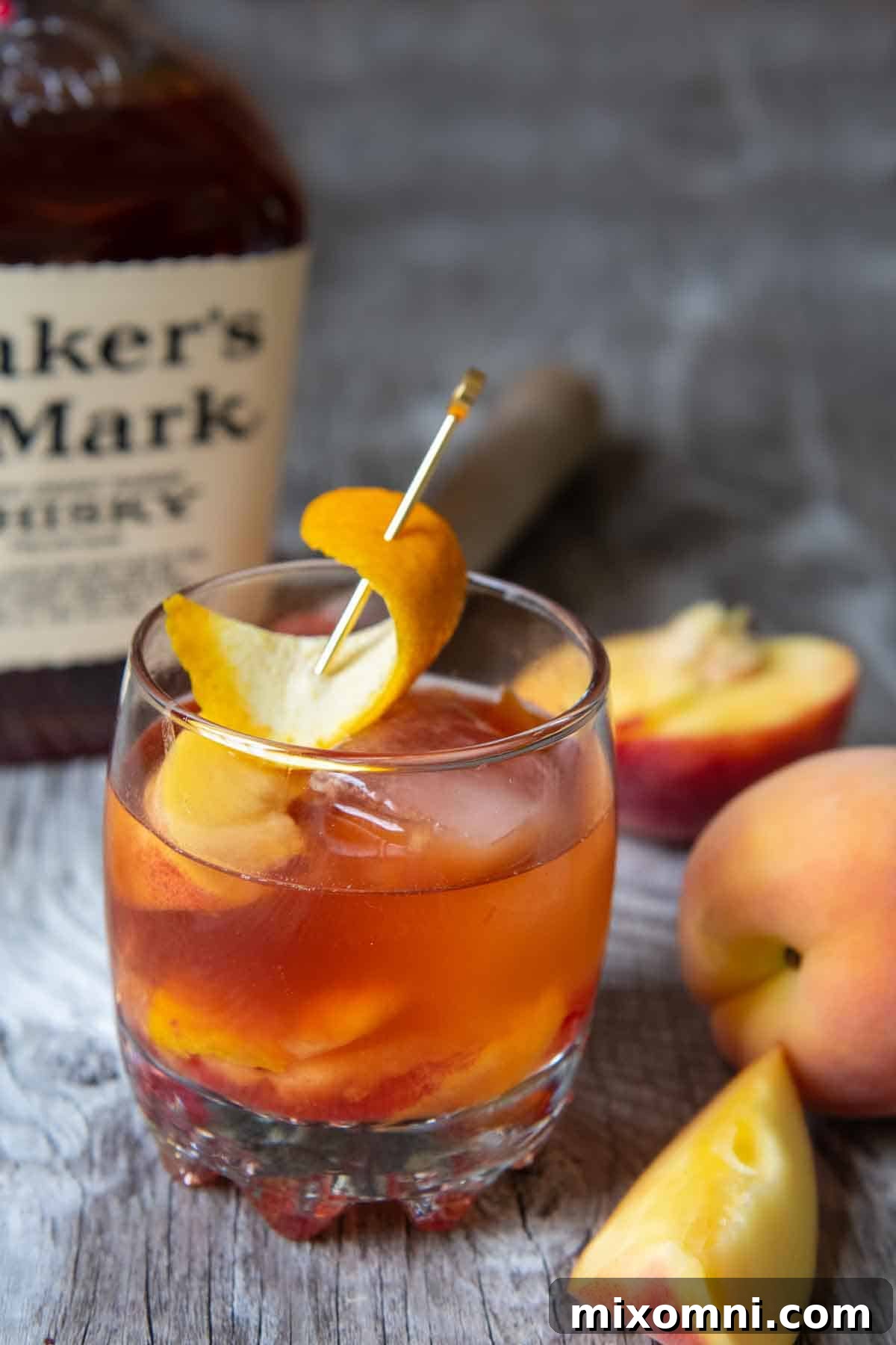 a peach old fashioned on a wood board with bourbon in the background