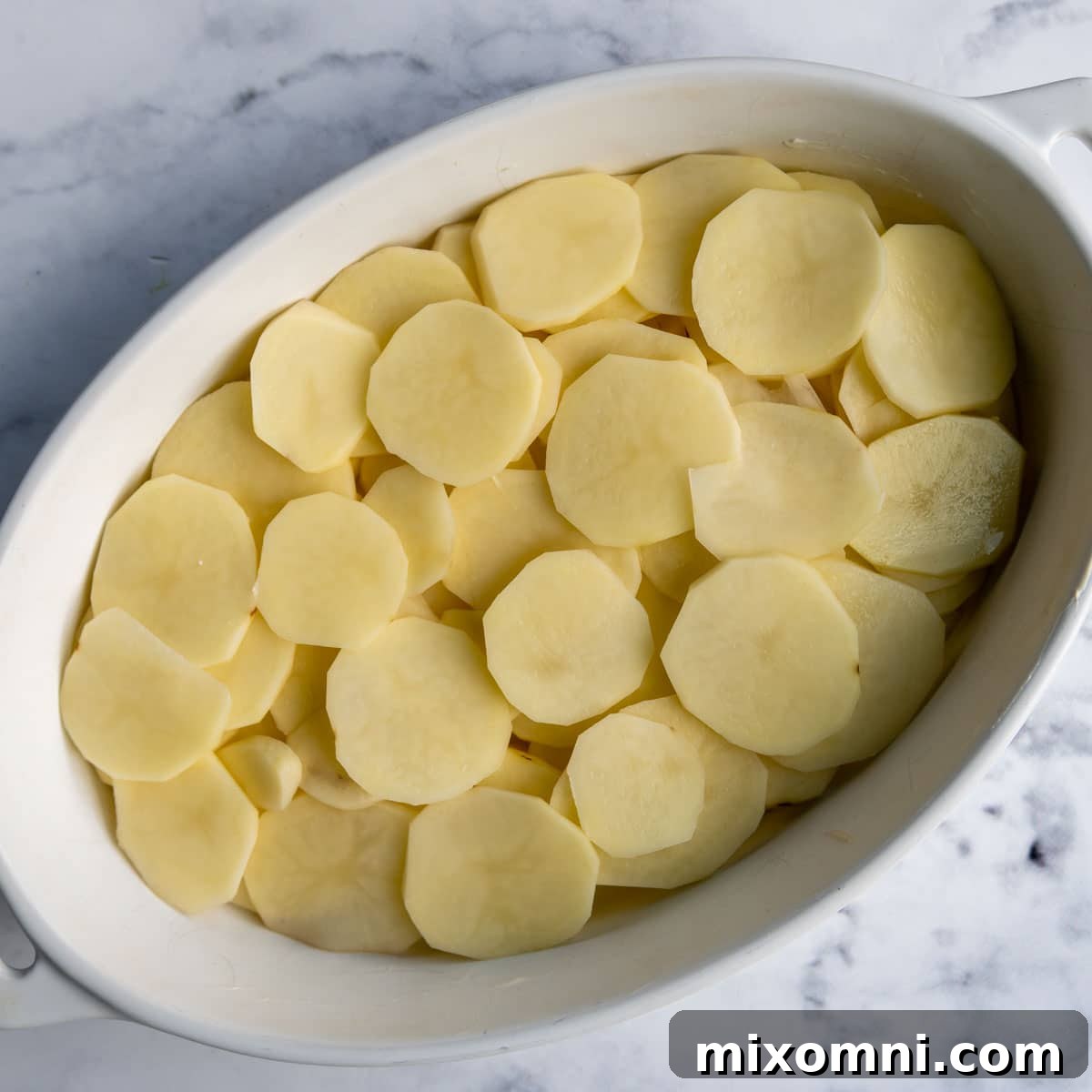 A bottom layer of neatly sliced, unbaked potatoes arranged in a greased baking dish, ready for the sauce.