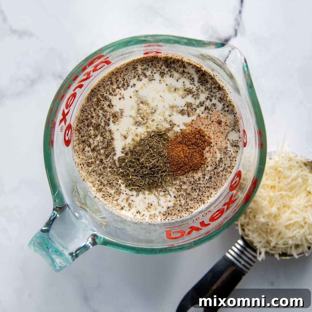 A bowl of creamy sauce, freshly grated Swiss cheese, and Parmesan cheese, ready to be layered into the potato dish.