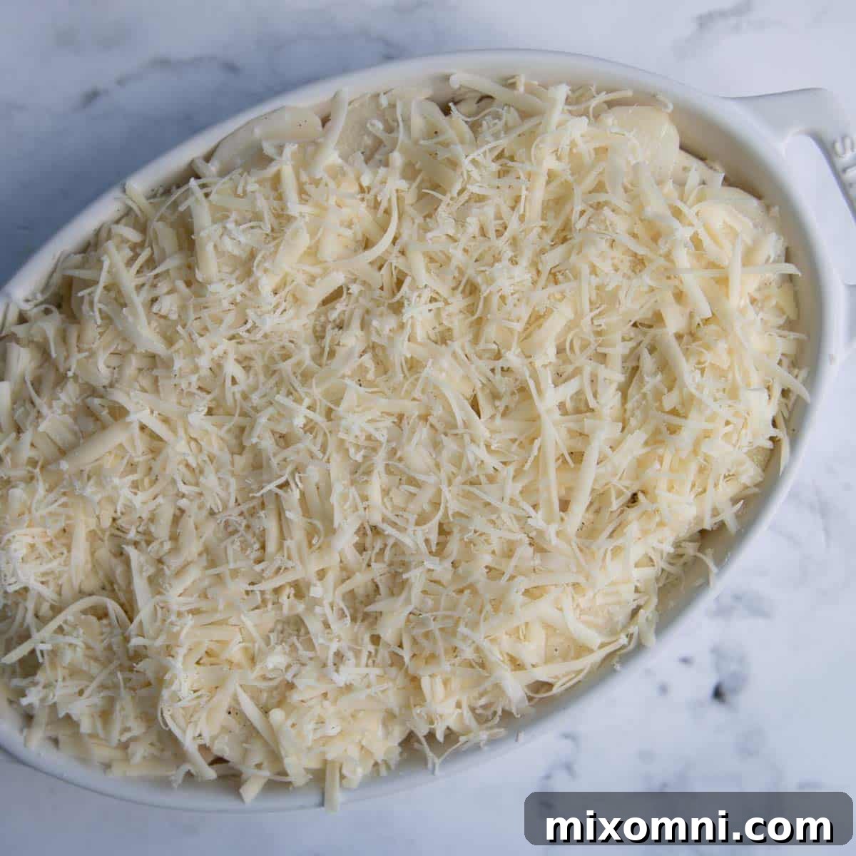 An unbaked au gratin potato dish, showing multiple layers of thinly sliced potatoes, cream sauce, and grated cheeses.
