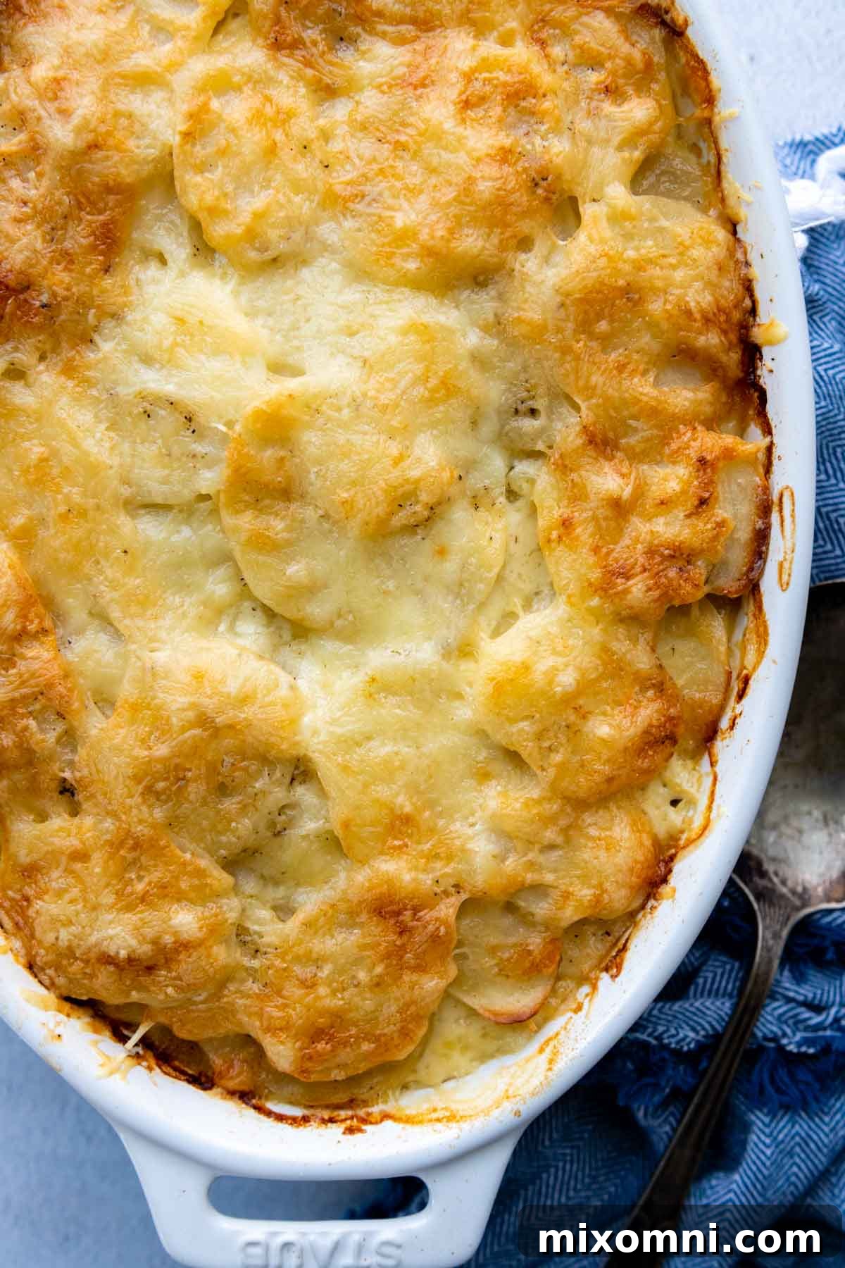 An overhead shot of a white casserole dish filled with unbaked layered potatoes, accompanied by a blue patterned kitchen towel.