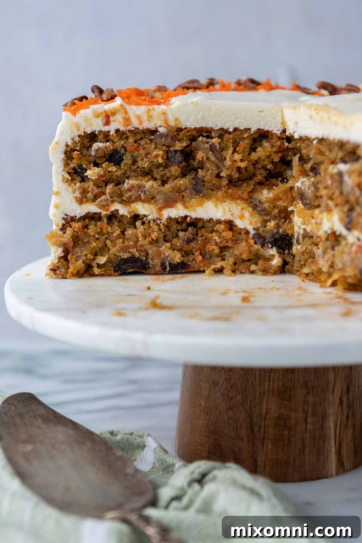 layered carrot cake on a cake stand with a large slice missing.