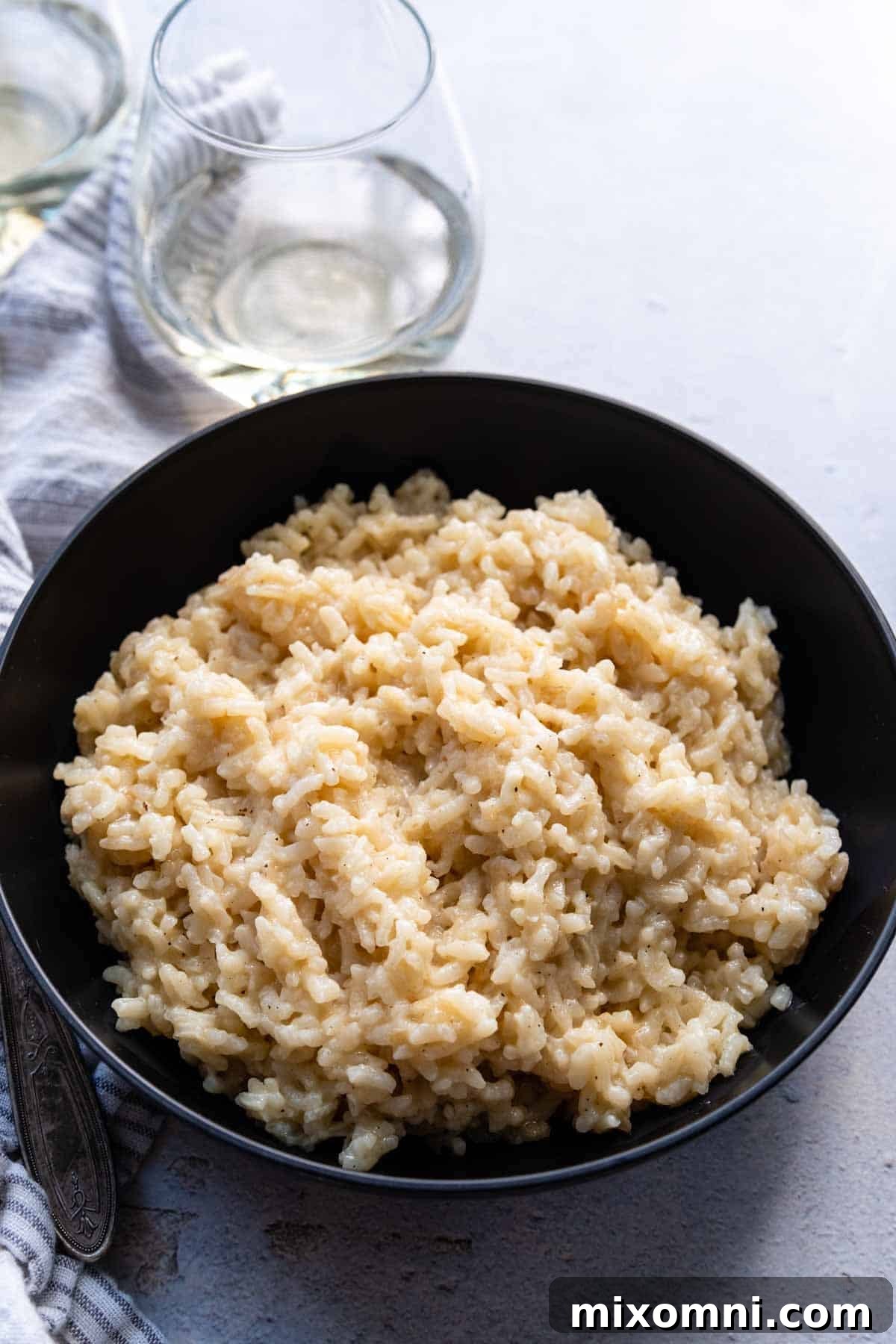 Creamy gluten-free risotto in a black bowl, with elegant wine glasses softly blurred in the background, creating an inviting culinary scene.