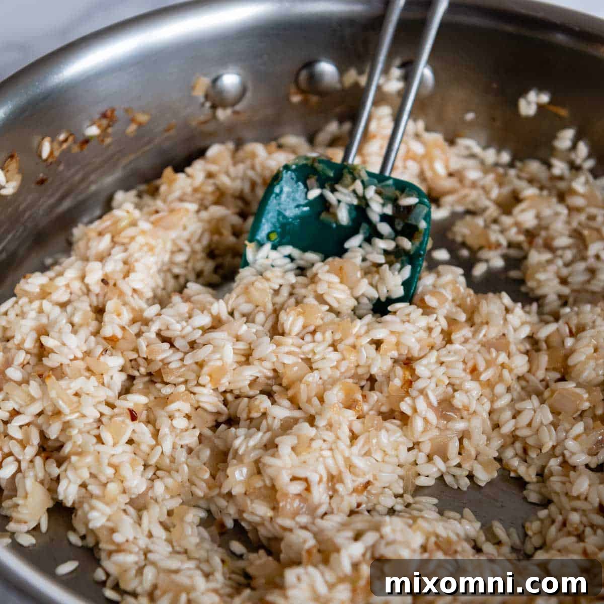Gluten-free Arborio rice and dry white wine added to the pan with sautéed shallots, being stirred to combine.