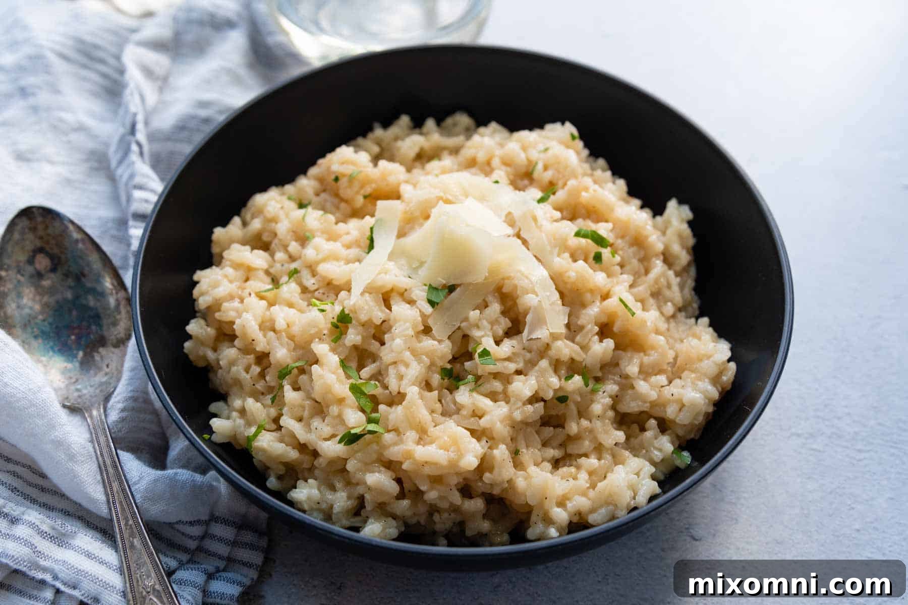 A close-up of creamy gluten-free risotto in a black bowl, garnished with a generous sprinkle of fresh Parmesan cheese.