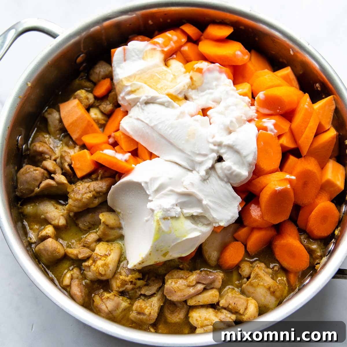 Rich coconut milk being poured into the skillet with chicken and vegetables, creating the creamy base for the gluten-free curry.