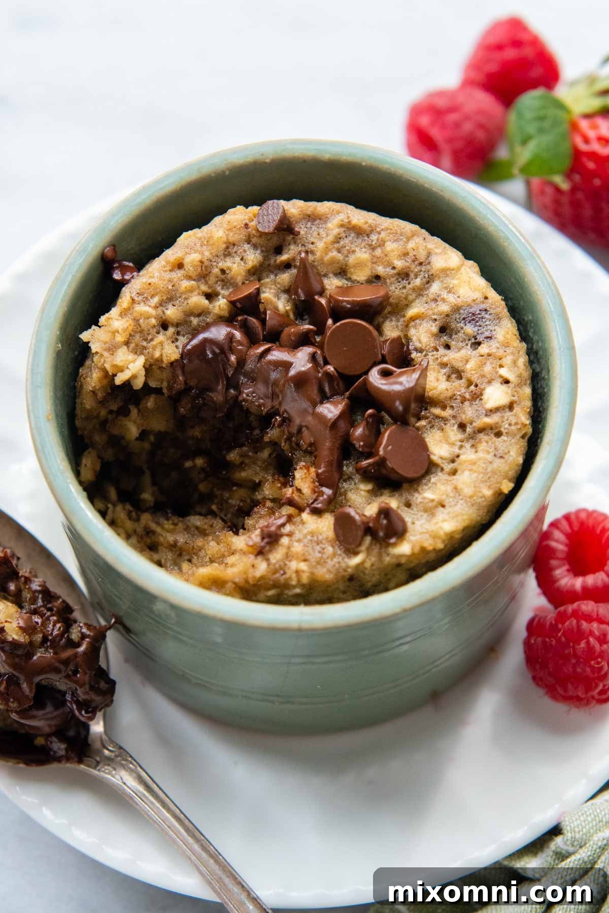A bite taken out of a fluffy oatmeal mug cake, with a spoon resting beside it, indicating its delicious texture and single-serving convenience.