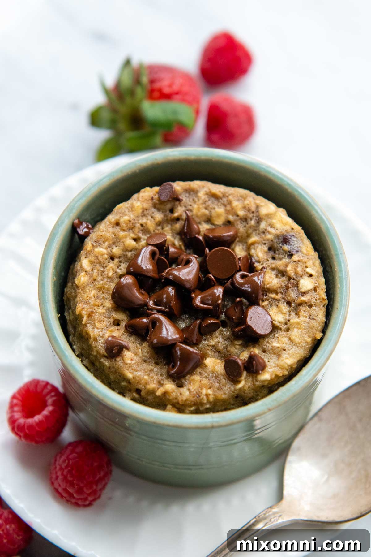 Overhead shot of an oatmeal mug cake served in a green dish, surrounded by fresh berries.