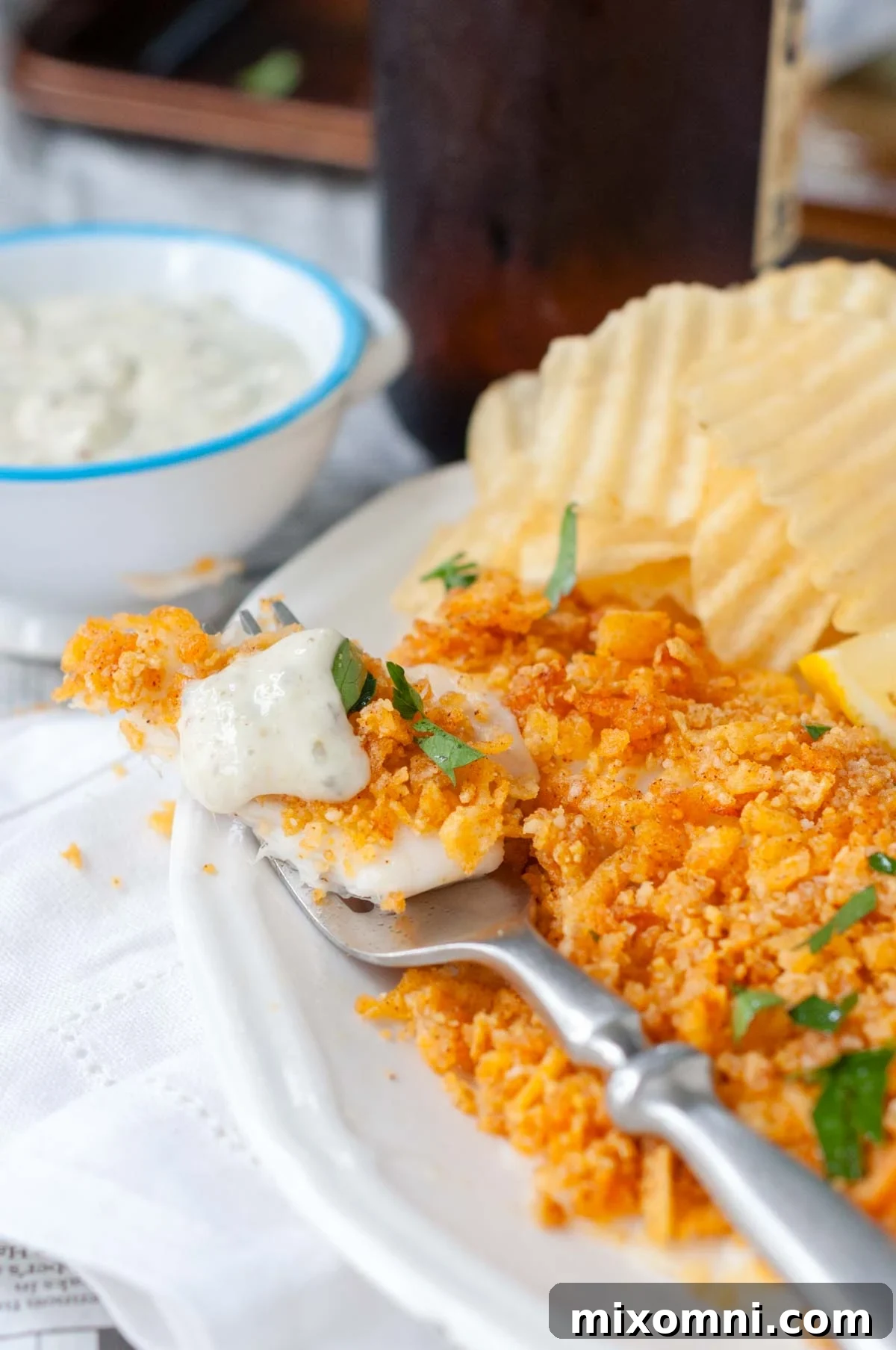 A fork with a bite of golden-brown crispy gluten-free fish, topped with creamy tartar sauce.