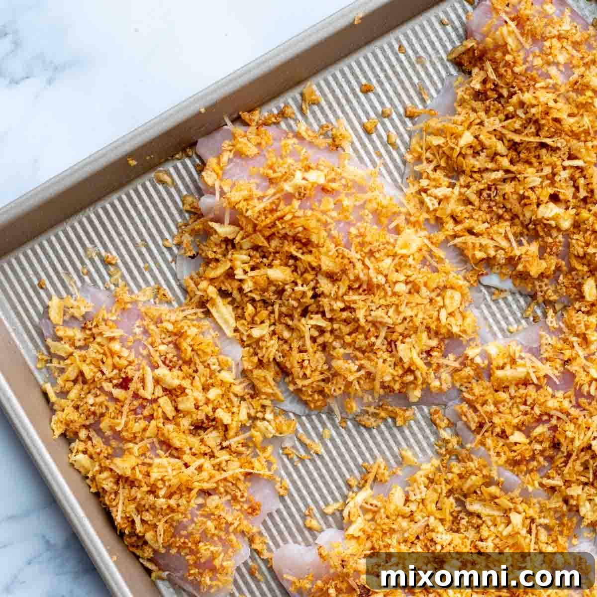 Unbaked fish fillets with the crispy topping evenly sprinkled over them on a baking sheet.