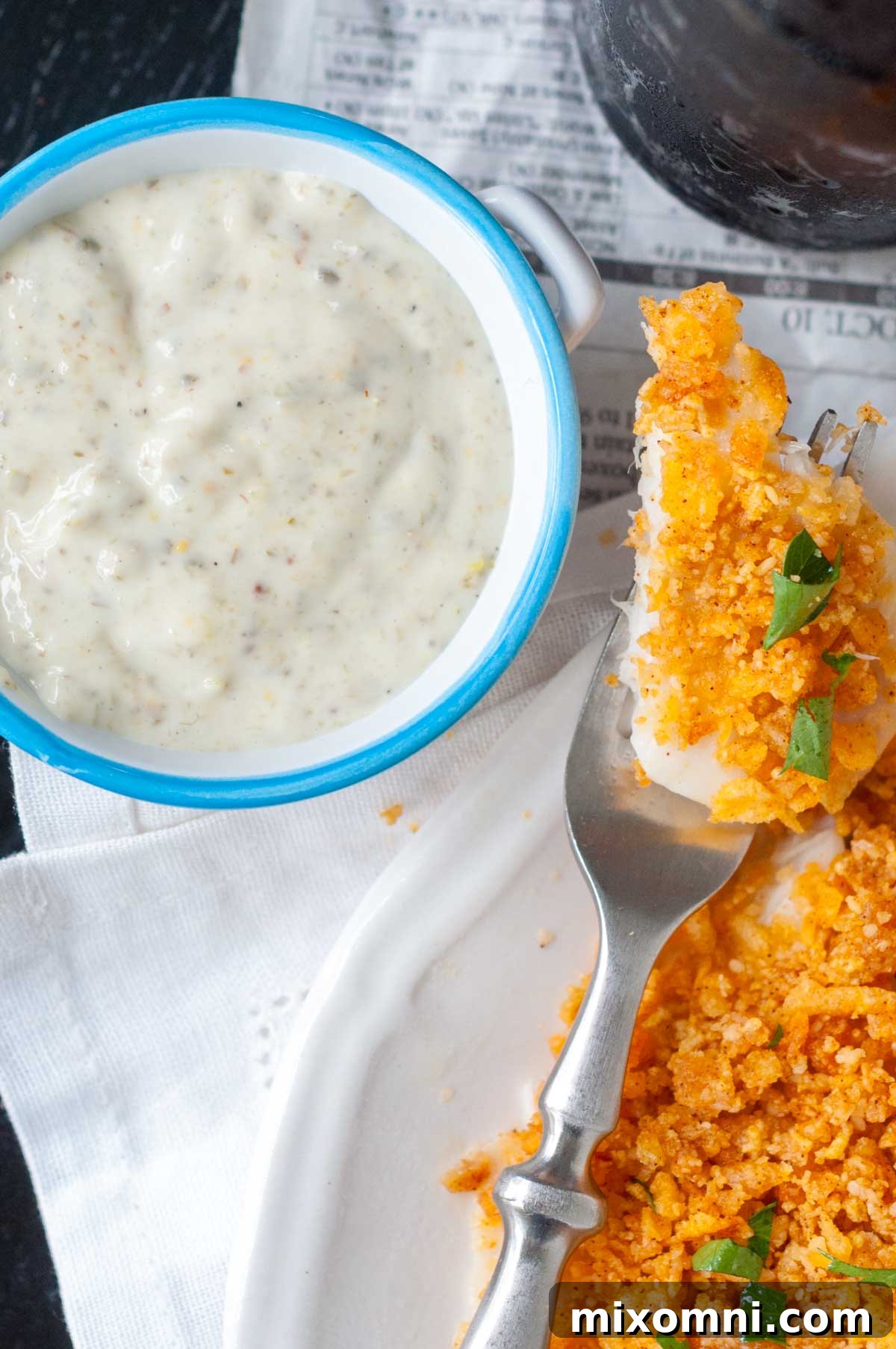 An overhead shot of a small bowl of creamy homemade tartar sauce with a perfectly baked, crispy fish fillet next to it.