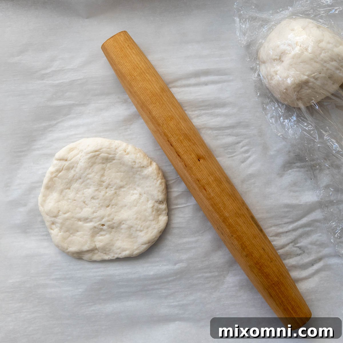 A ball of gluten-free dough flattened into a thick disc on parchment paper, ready for rolling.