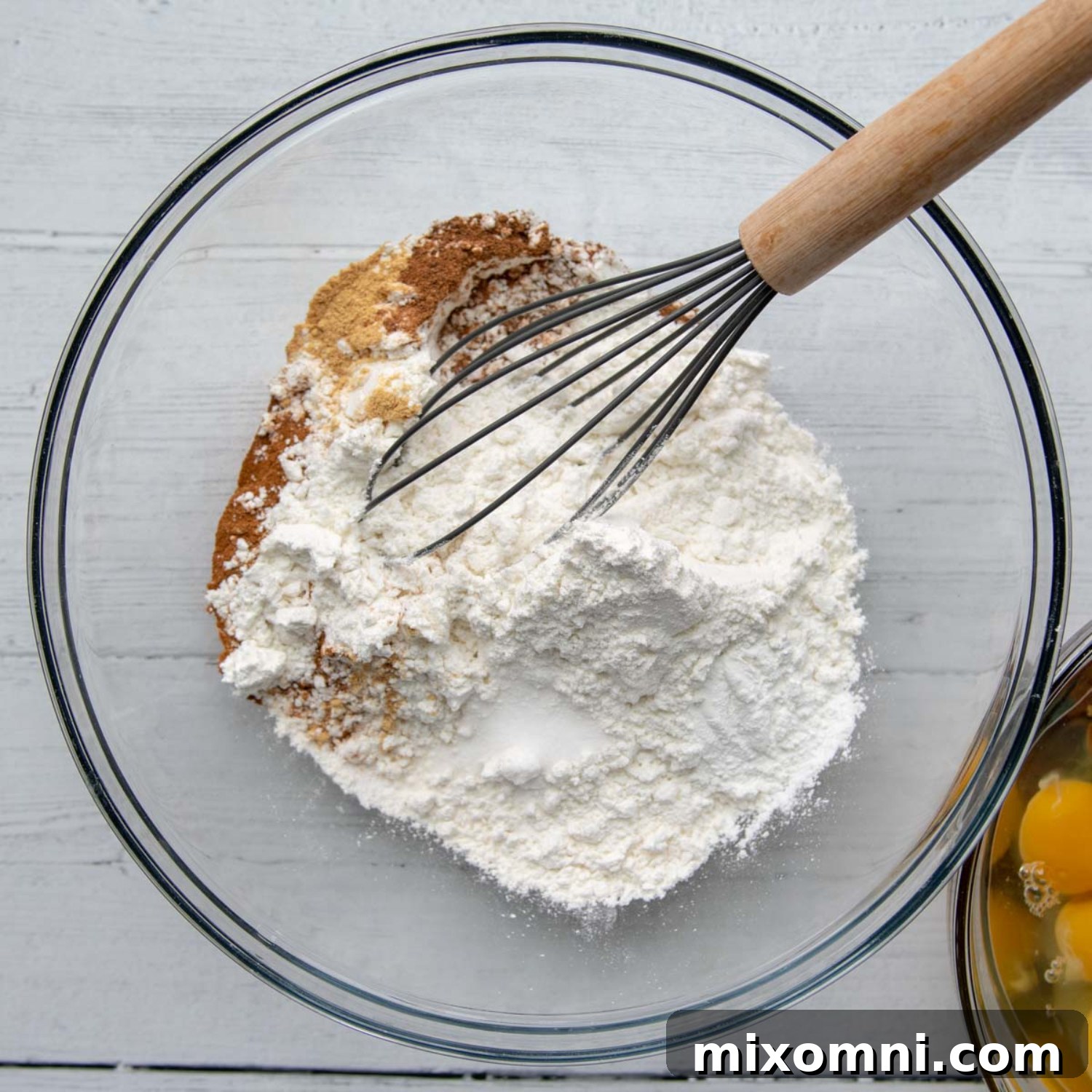 Dry ingredients in a large glass bowl with a whisk inside, ready for mixing.
