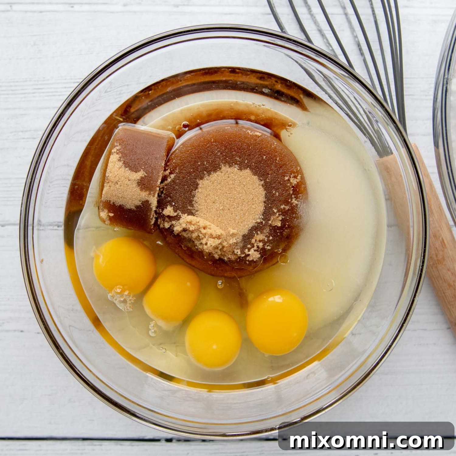 Wet ingredients including oil, sugar, and eggs in a separate large glass bowl, whisked together.