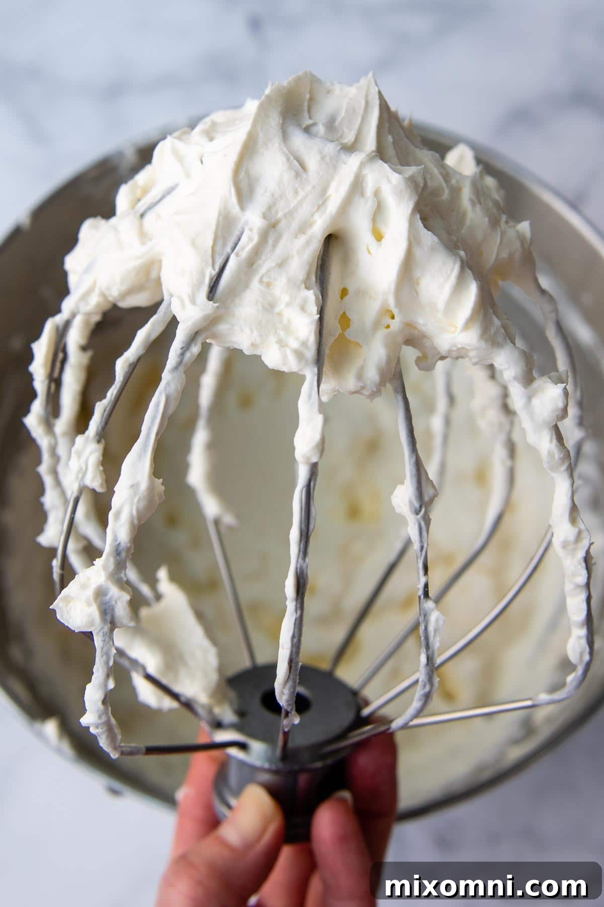 A beater covered in luxurious, fluffy cream cheese frosting, ready to be spread.