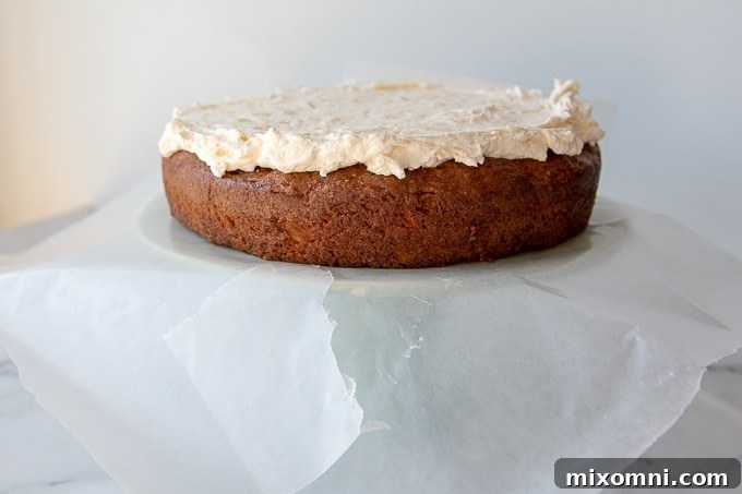 One layer of moist carrot cake on a cake stand getting frosted with creamy white frosting.