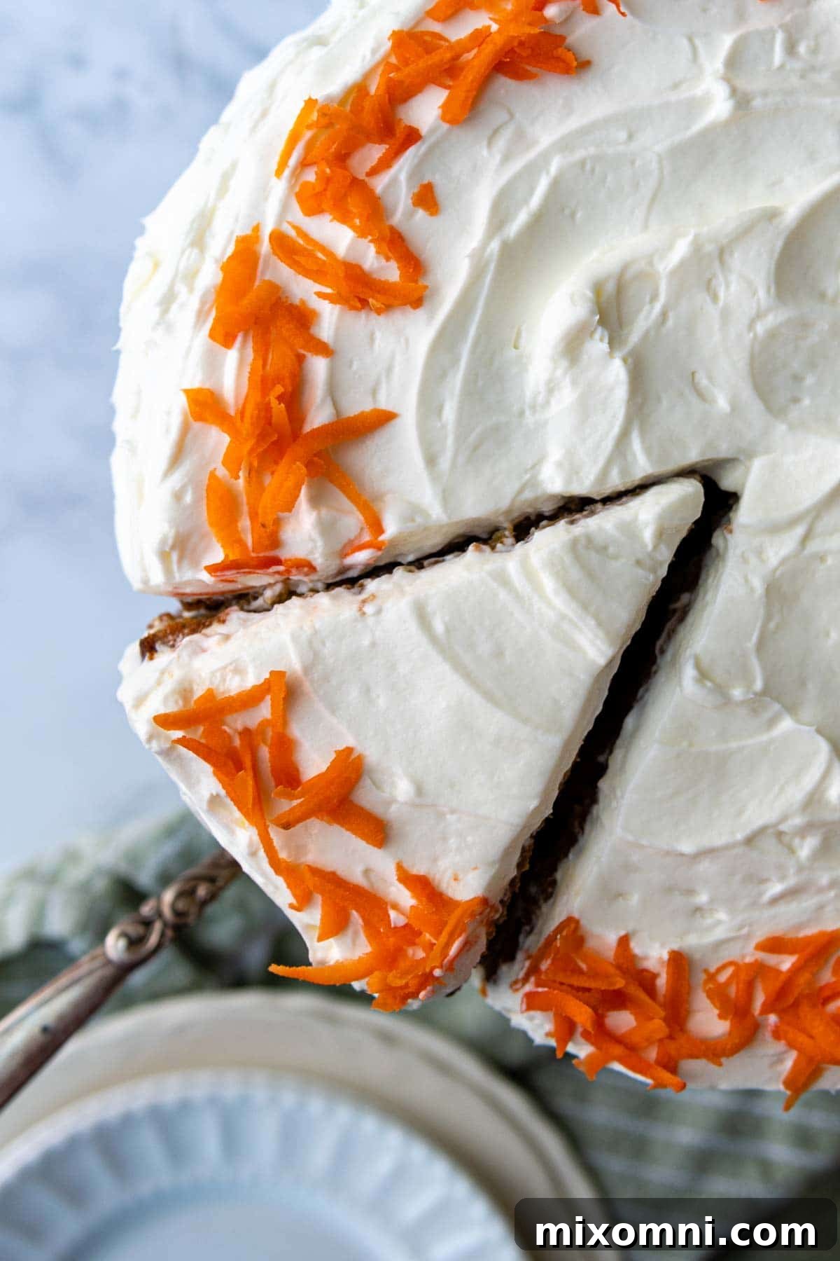 Overhead shot of a gloriously frosted carrot cake with fluffy whipped cream cheese frosting and shredded carrots on top.