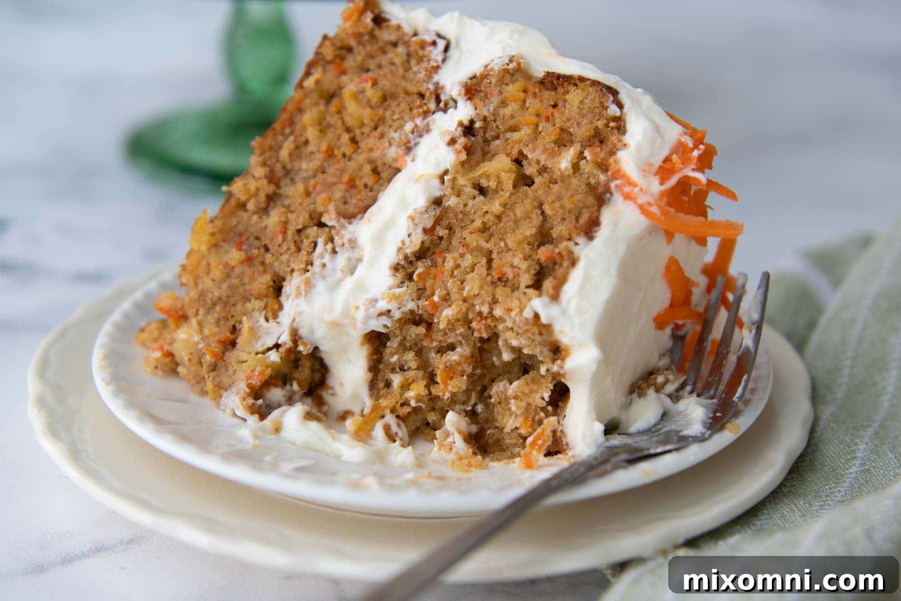 A perfectly portioned slice of moist carrot cake on a white plate with a bite taken out, showing the tender crumb and frosting layers.