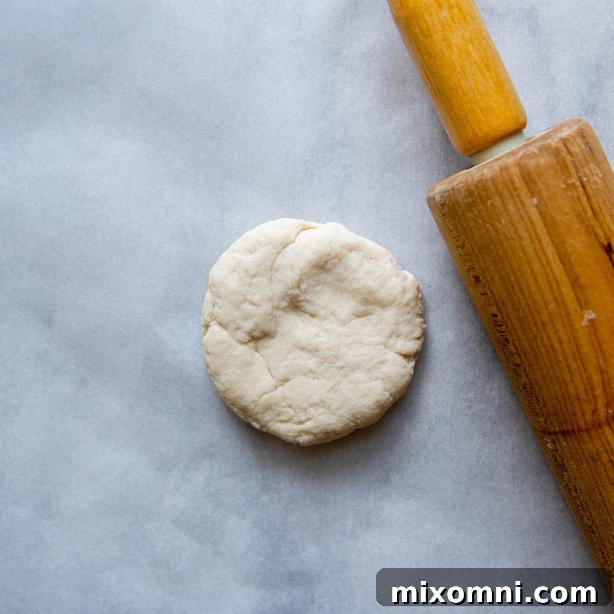 A thick disc of gluten-free dough ready for rolling, with a rolling pin beside it, symbolizing the start of tortilla creation.