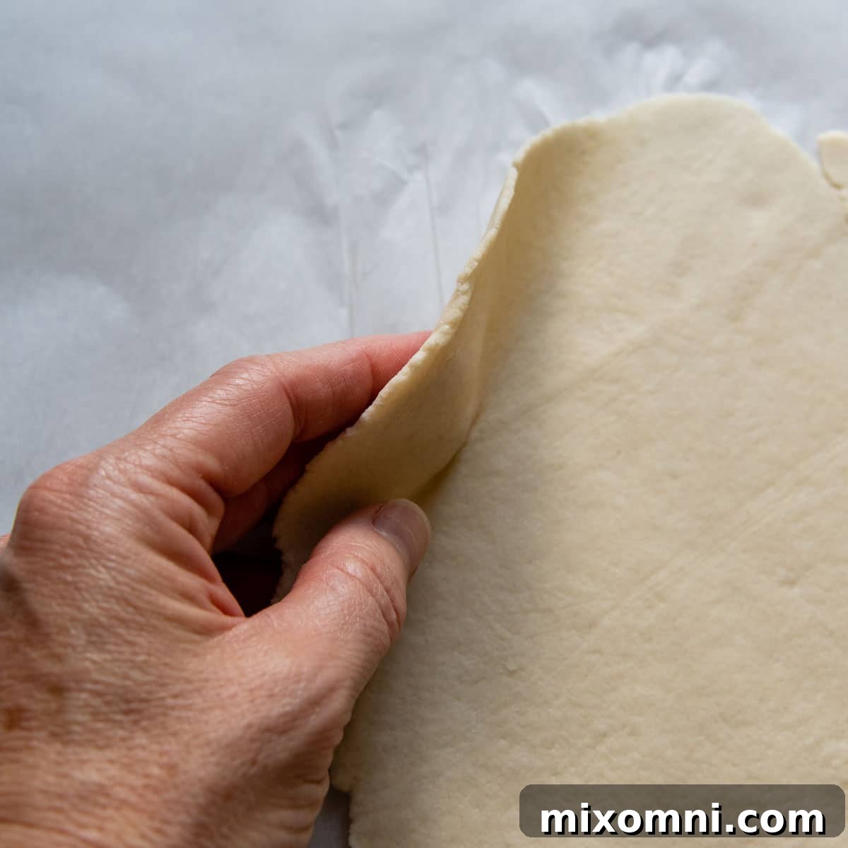 A hand demonstrating the thin, consistent thickness of the rolled gluten-free dough, ensuring even cooking.