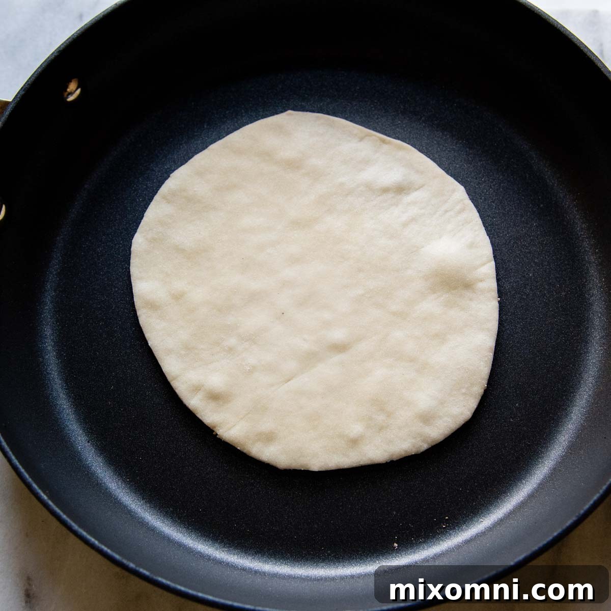 A gluten-free tortilla cooking in a hot skillet, showing the beginning of light browning and bubbling.