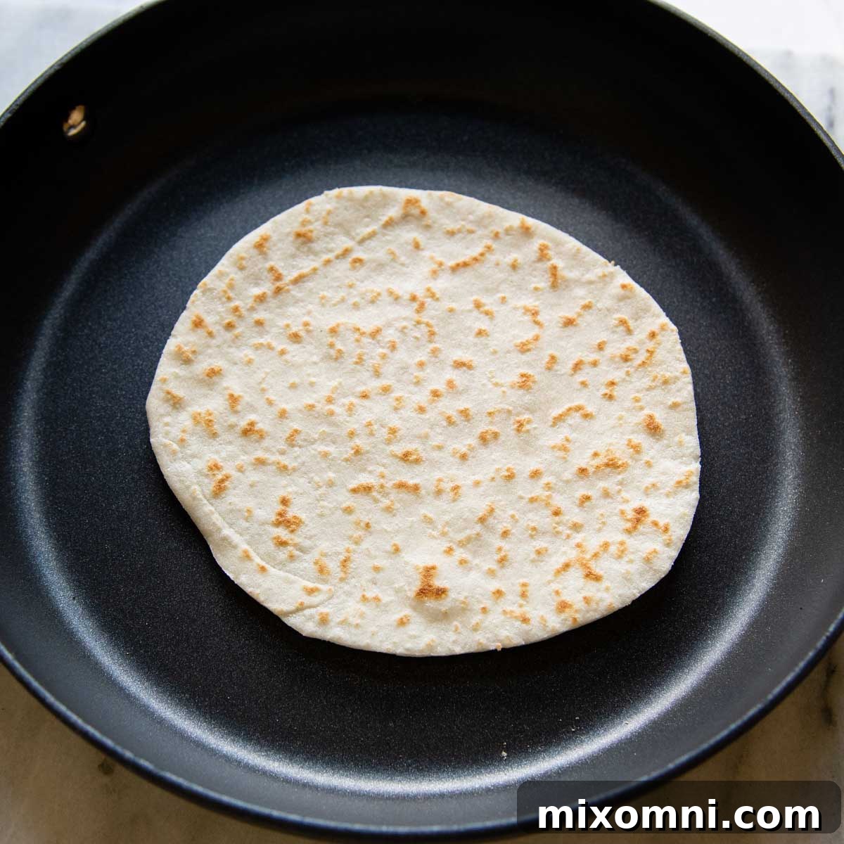 A gluten-free tortilla sizzling in a skillet after being flipped, showcasing its golden-brown underside.