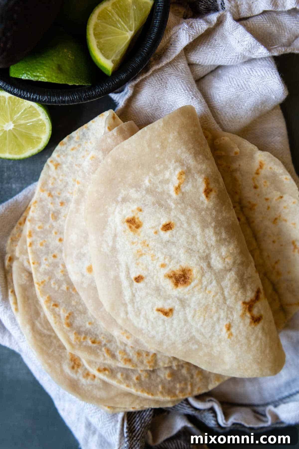 Several soft, folded gluten-free tortillas artfully arranged with a fresh lime wedge, suggesting a delicious meal.