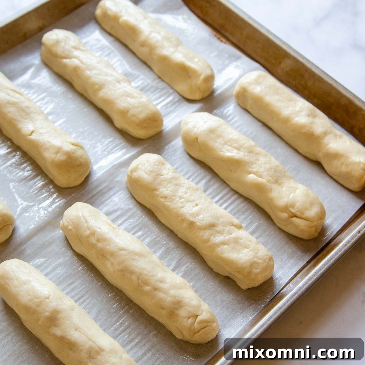 Gluten-free hot dog bun dough rolled into smooth logs and arranged on a baking sheet, ready for proofing.