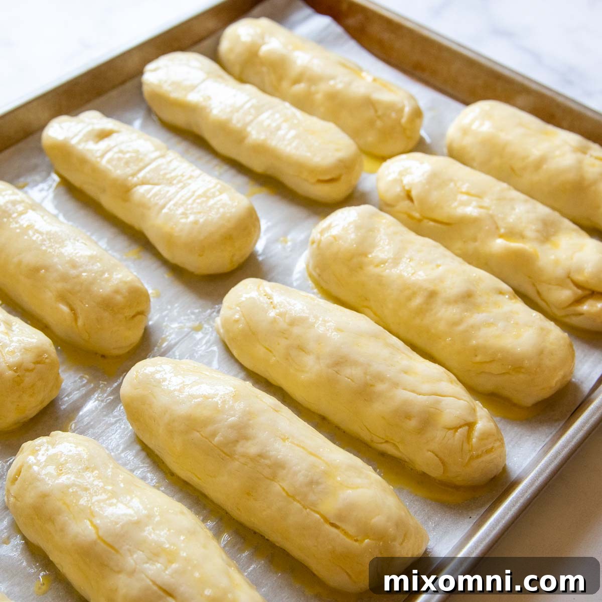 Freshly risen gluten-free hot dog buns brushed with egg wash and ready for baking, showcasing their potential for a golden, fluffy finish.