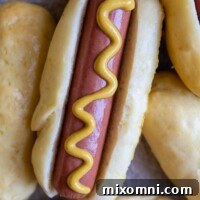 A hot dog with mustard on it resting next to other fluffy, soft gluten-free buns.