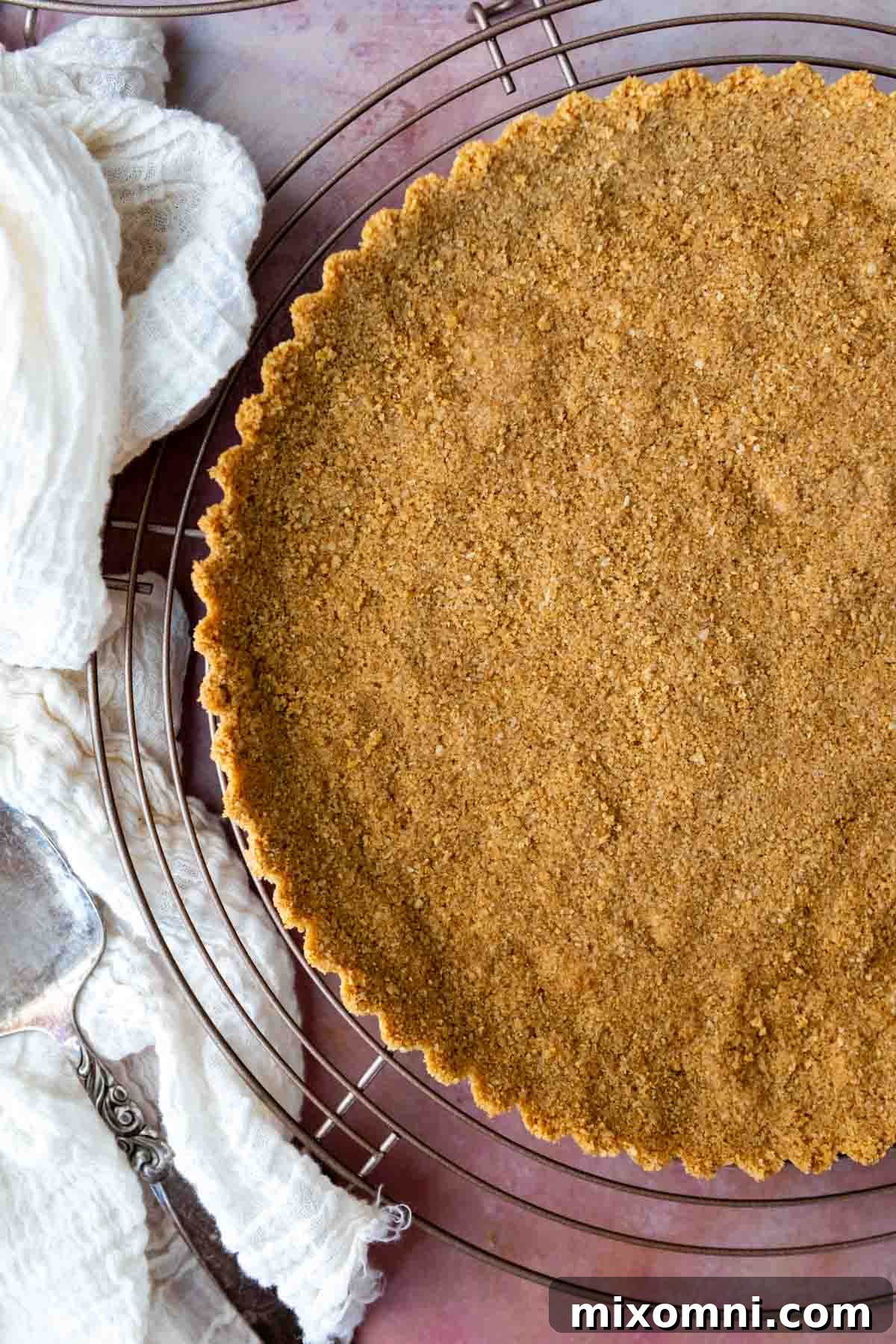 A golden brown gluten-free graham cracker crust cooling on a wire rack next to a kitchen towel, showcasing its perfect texture and stability.