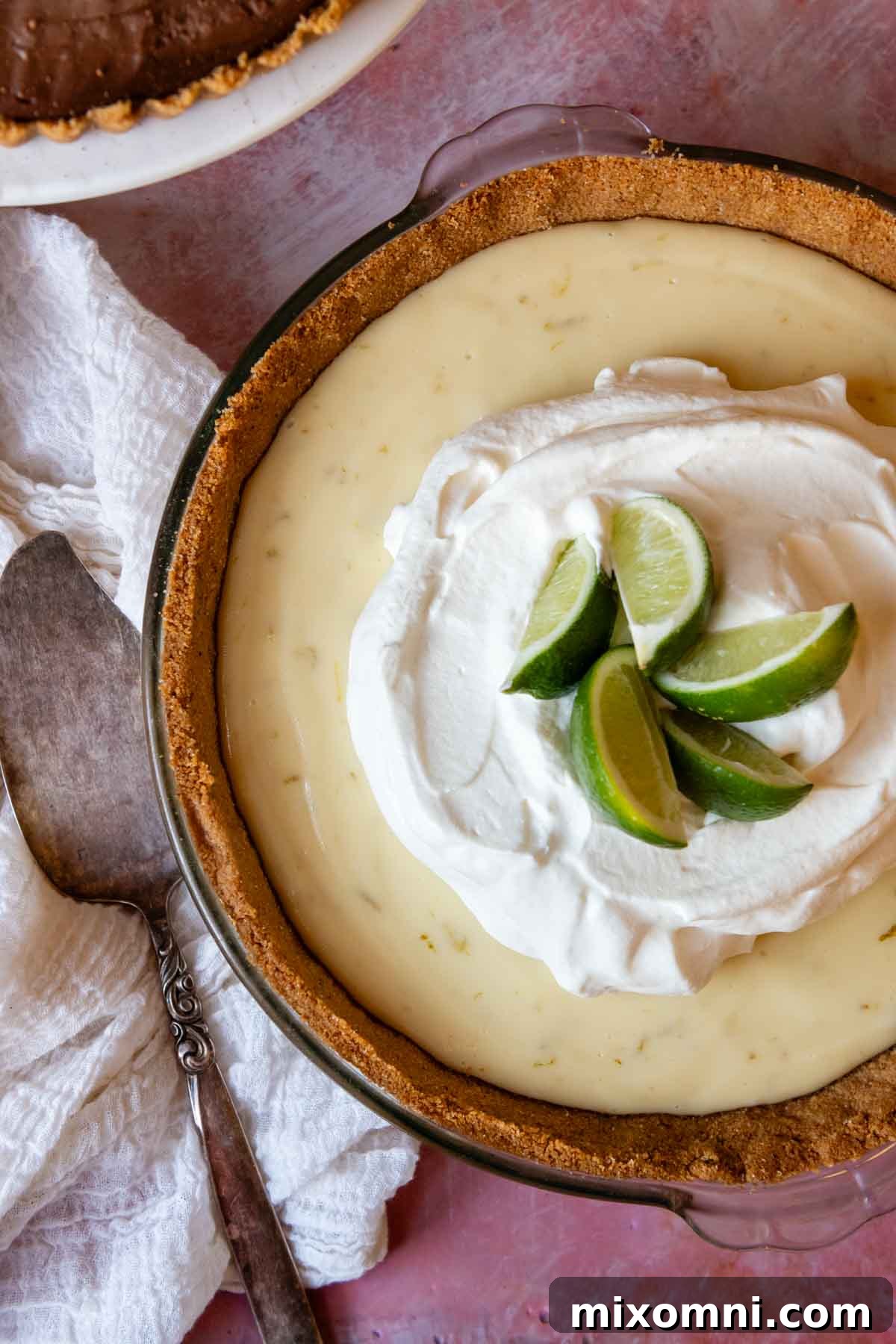 An overhead shot of a vibrant key lime pie, nestled in a gluten-free graham cracker crust, presented on a cheerful pink background.