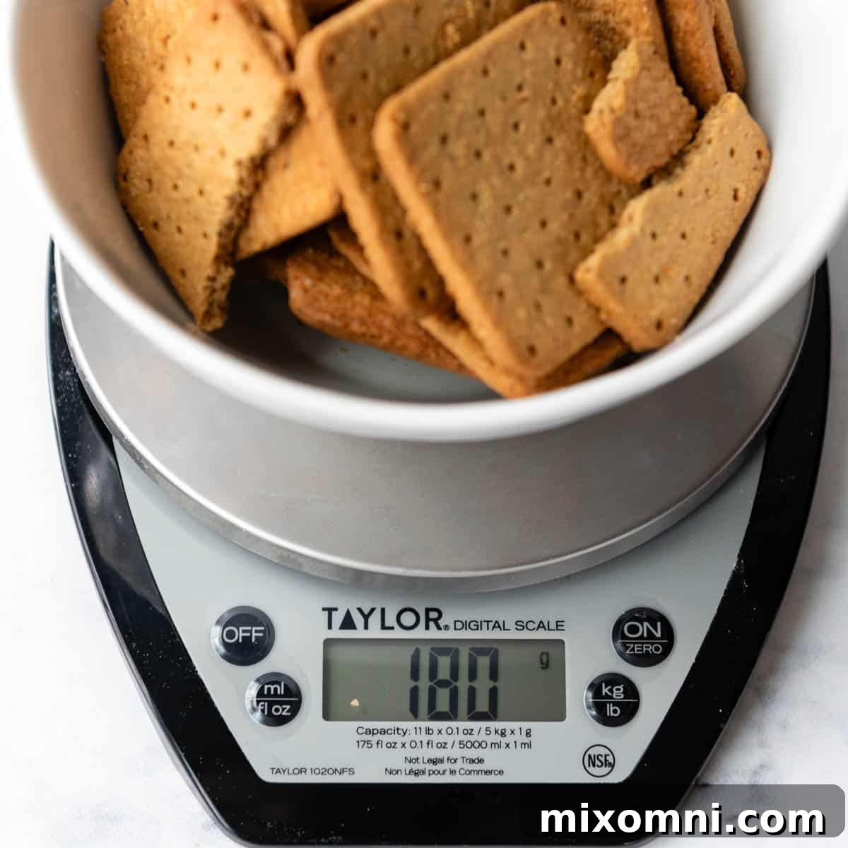A food scale accurately measuring gluten-free graham crackers, emphasizing the importance of precise ingredient measurements for a perfect crust.