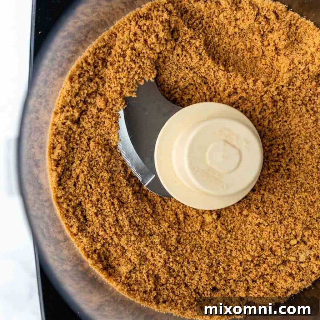 Gluten-free graham cracker crumbs being processed to a fine consistency in a food processor.