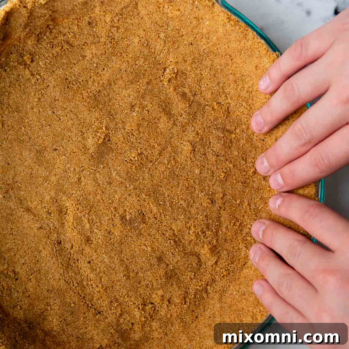 Fingers gently pressing the graham cracker mixture up the sides of the pie plate, forming a neat and sturdy crust edge.