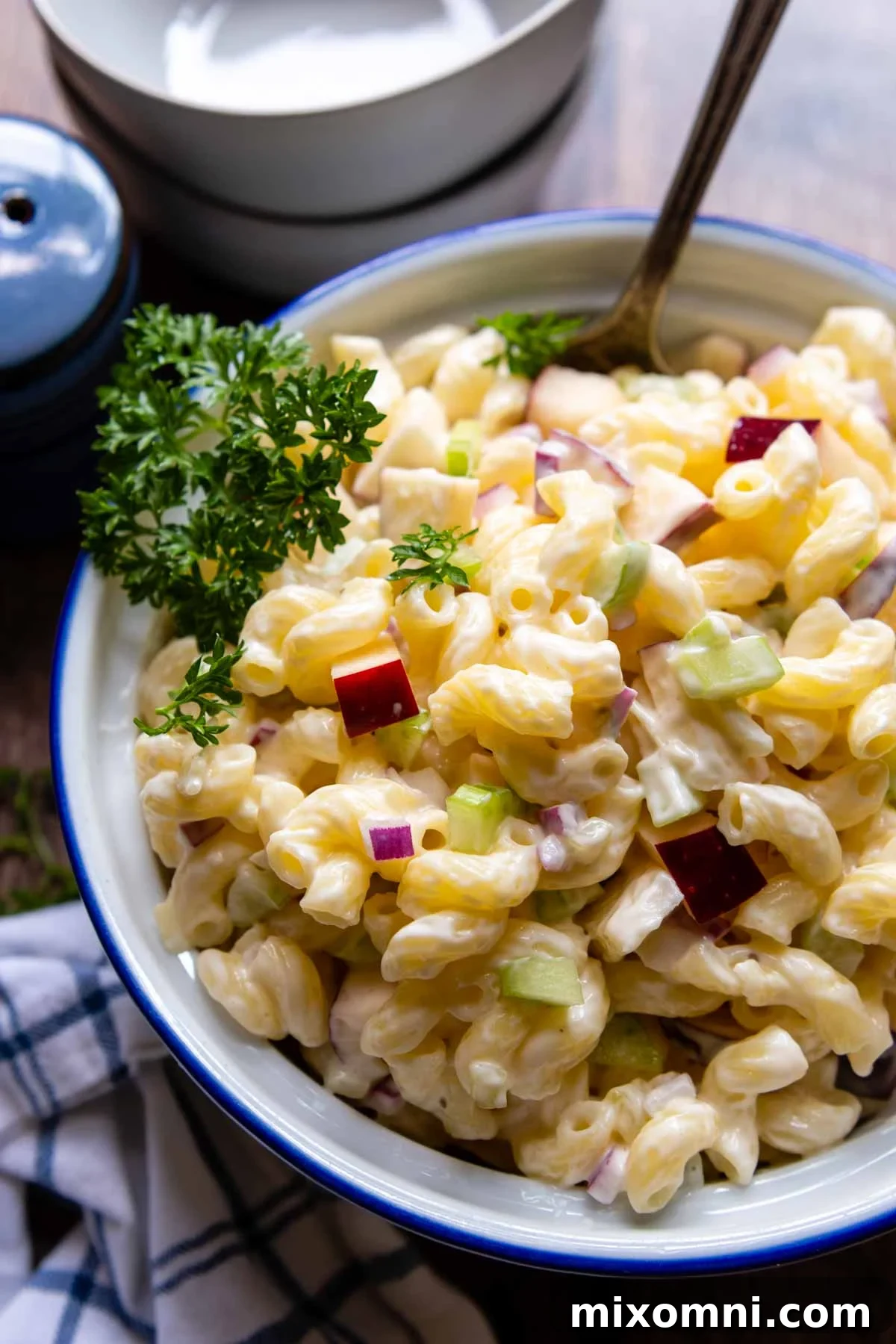 A spoon dipping into a bowl of creamy gluten-free macaroni salad, garnished with fresh parsley.